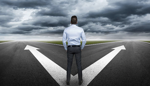 A man standing on a road with arrows facing in two different directions.