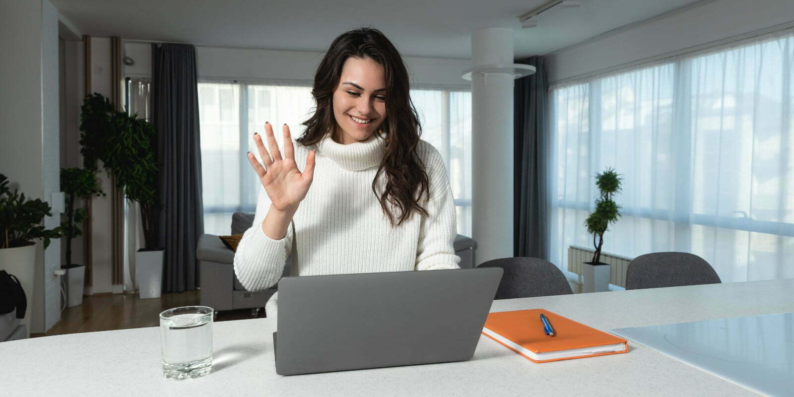A person sitting at a computer smiling and waving at the screen.