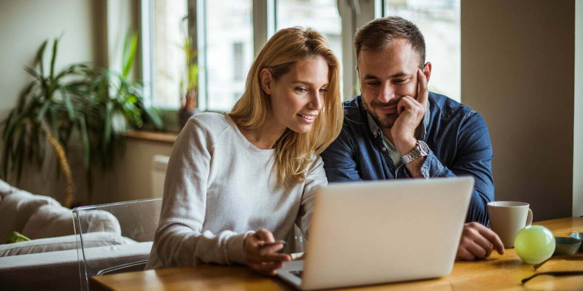 A couple sitting at a table looking at a computer smiling.