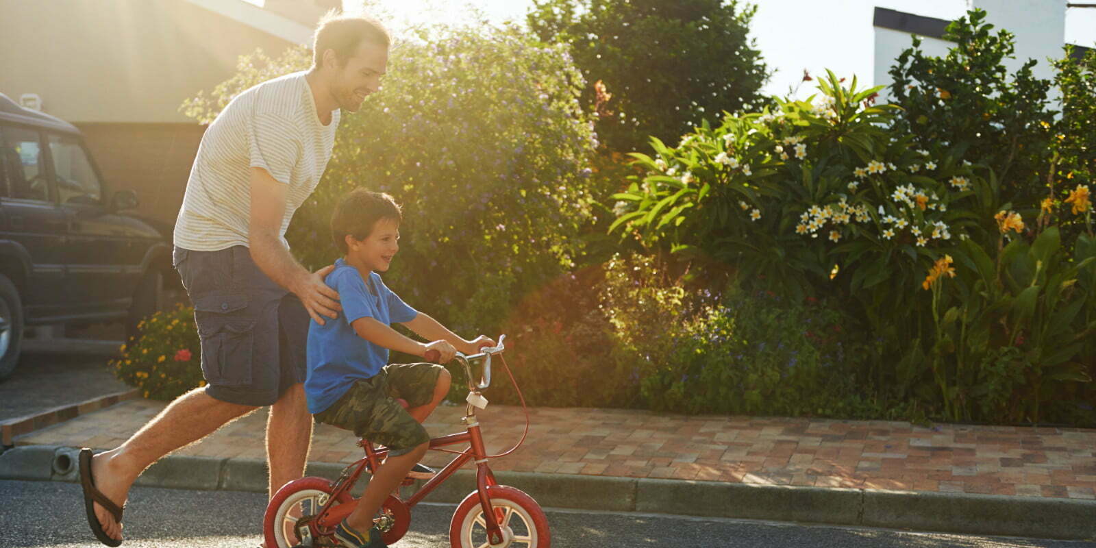 A young boy learning to ride bicycle as father teaches him in the suburb street having fun.