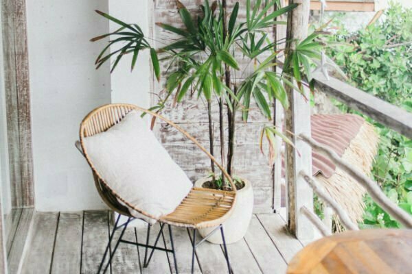 A comfortable cain seat with a cushion sitting on a stylish outdoor balcony.