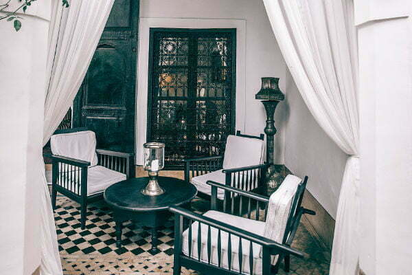 An inside seating arrangement with a lamp sitting in the middle of a table with three comfortable chairs.