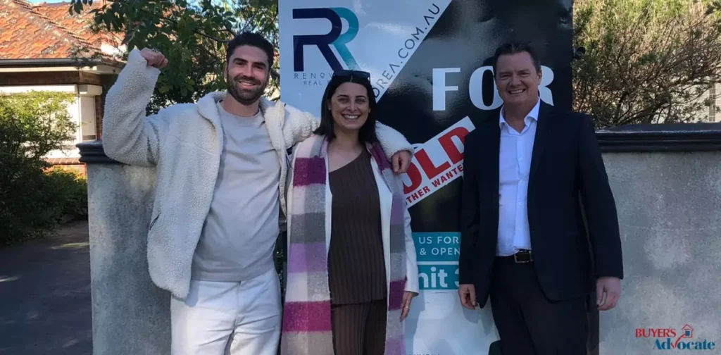 A smiling couple poses with their buyer’s advocate in front of a sold sign outside their new Melbourne home, marking a successful property purchase with Buyers Advocate Australia.