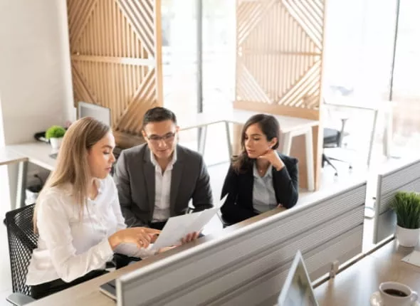 Three people reviewing property documents at a computer during a property analysis meeting.